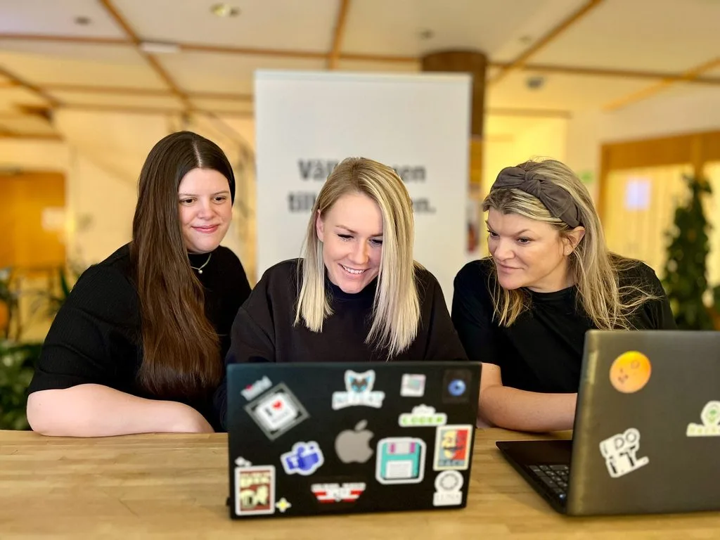Emma, Magdalena och Anna sitter samlade vid ett skrivbord och tittar ner i en laptop.