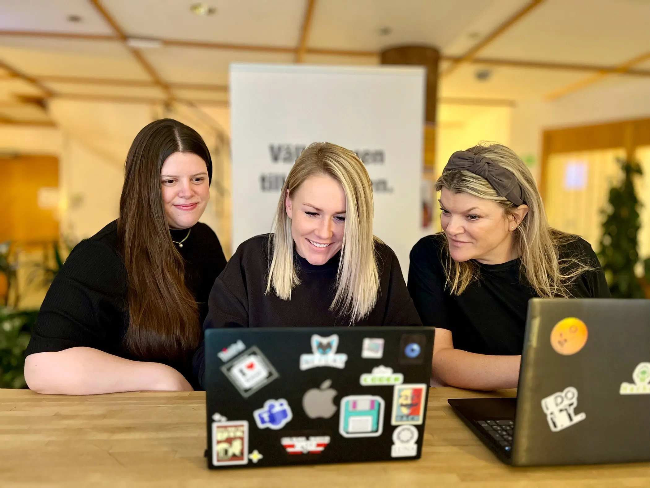 Emma, Magdalena och Anna sitter samlade vid ett skrivbord och tittar ner i en laptop.