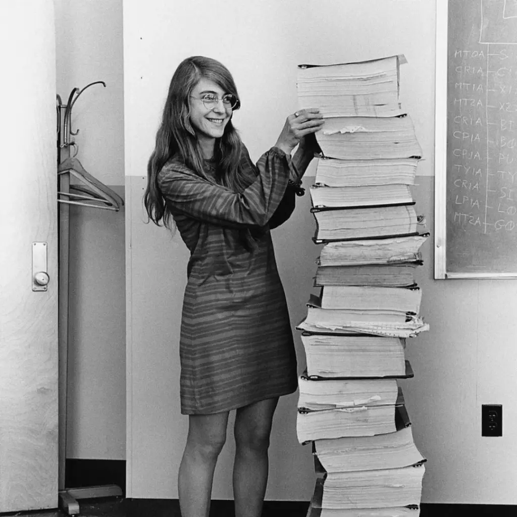 Margaret Hamilton vid en stor hög böcker. Bildkälla: NASA.