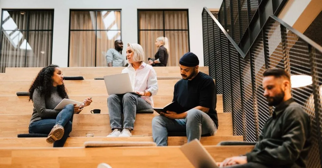 Grupp unga personer sitter på en trätrapp och diskuterar.