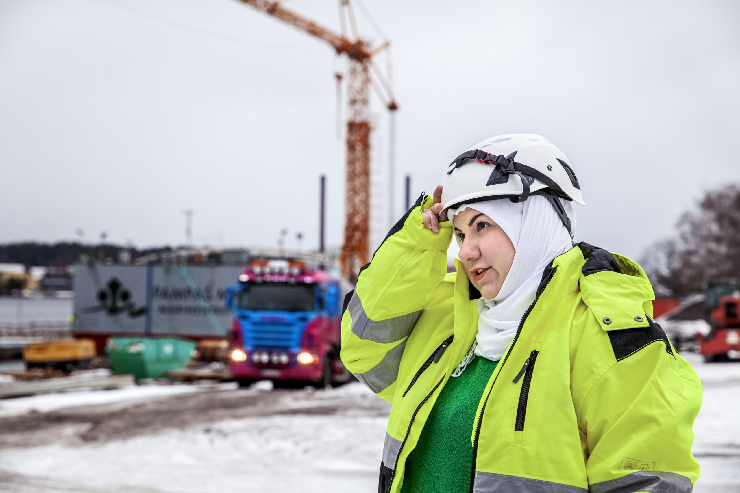 Kvinna med hjälm, hijab och varselkläder på byggarbetsplats