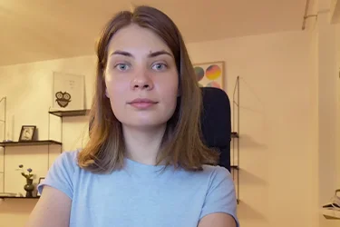 Irina Holm, tidigare studerande på Teknikhögskolan, med brunt axellångt hår och ljusblå topp sitter i en kontorsstol och tittar in i kameran.