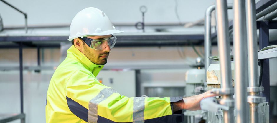 Man i varselställ och säkerhetsutrustning arbetar i en industrianläggning.