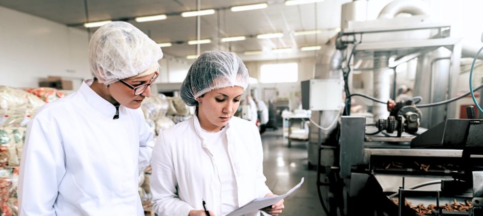 Två arbetare läser instruktioner i livsmedelsfabrik.