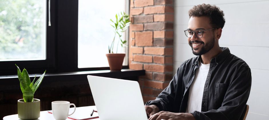 Man sitter och ler och tittar ner i en bärbar dator.