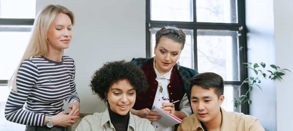 Fyra studerande samlade bakom ett bord och tittar ned på något.
